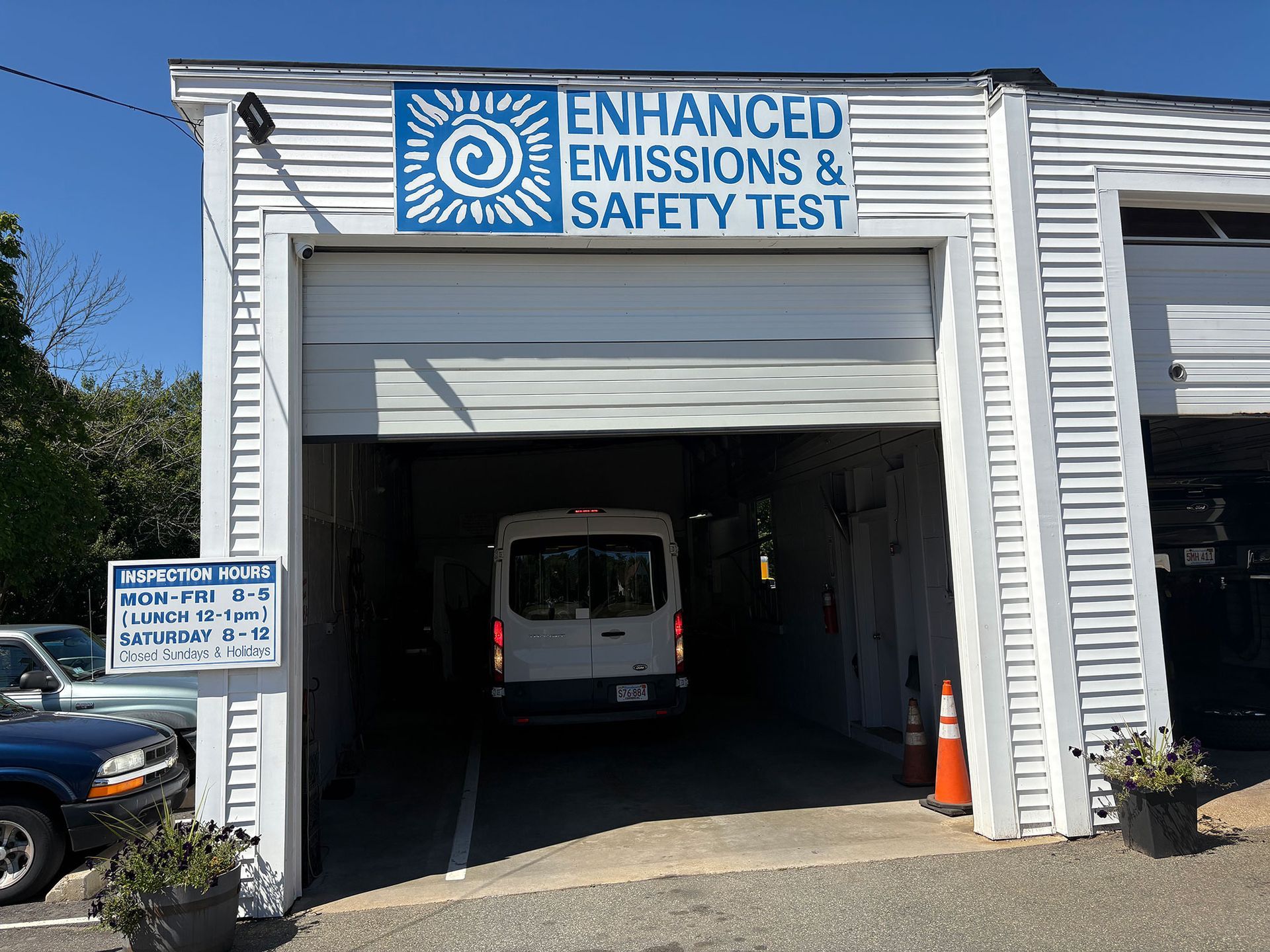 White van inside a building with a sign for emissions and safety tests; blue sky visible.