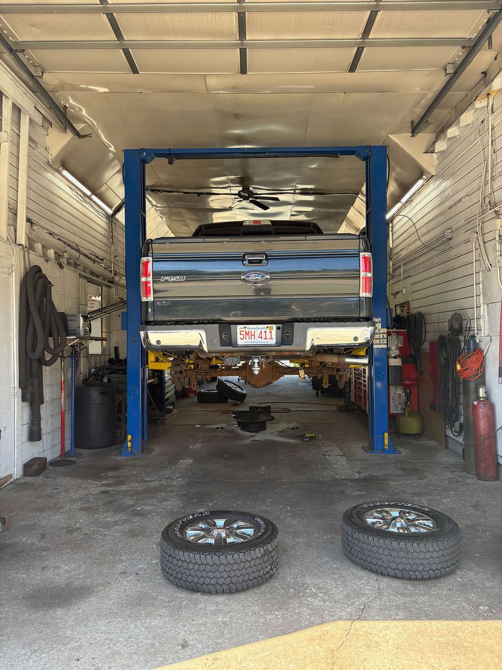 Truck on a lift in a garage; tires in the foreground.
