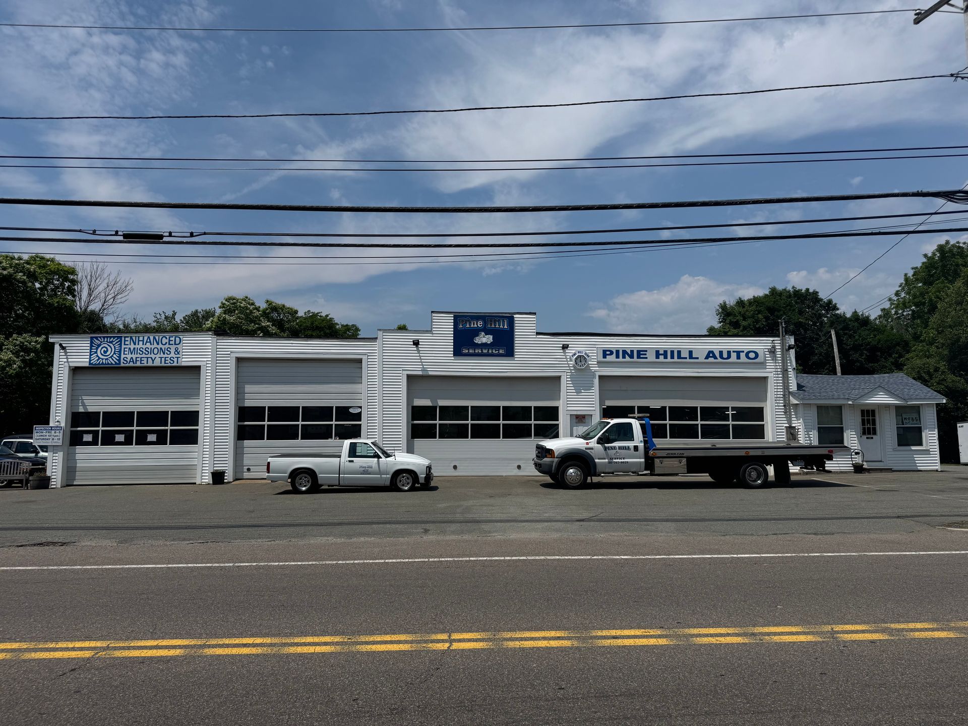 Pine Hill Auto repair shop with white trucks parked outside on a sunny day.