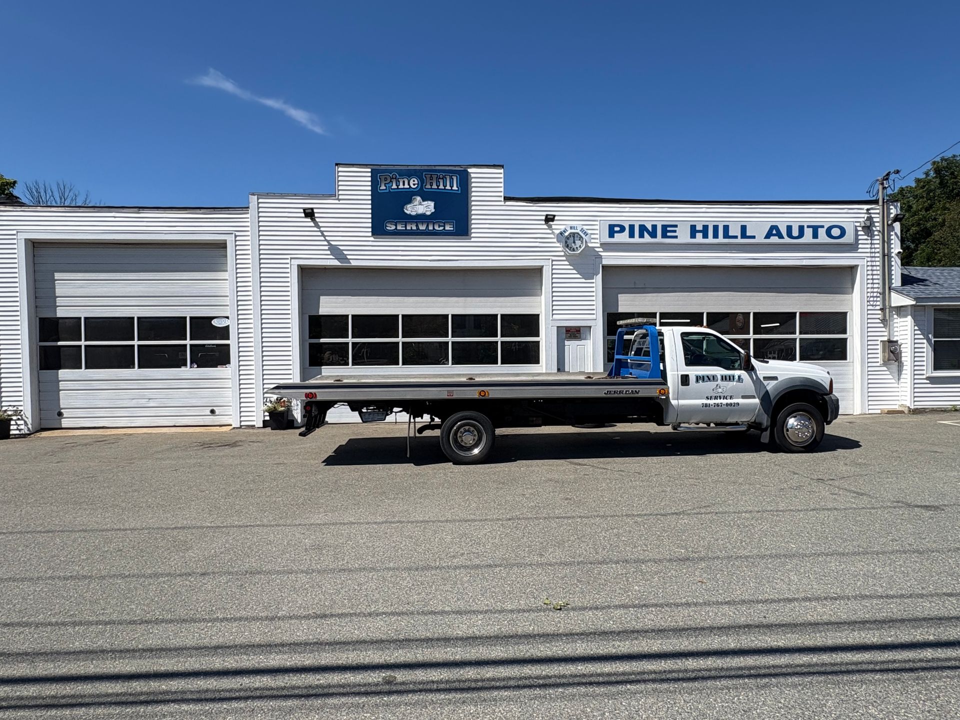 A white Pine Hill Auto garage with a tow truck parked out front on a sunny day.