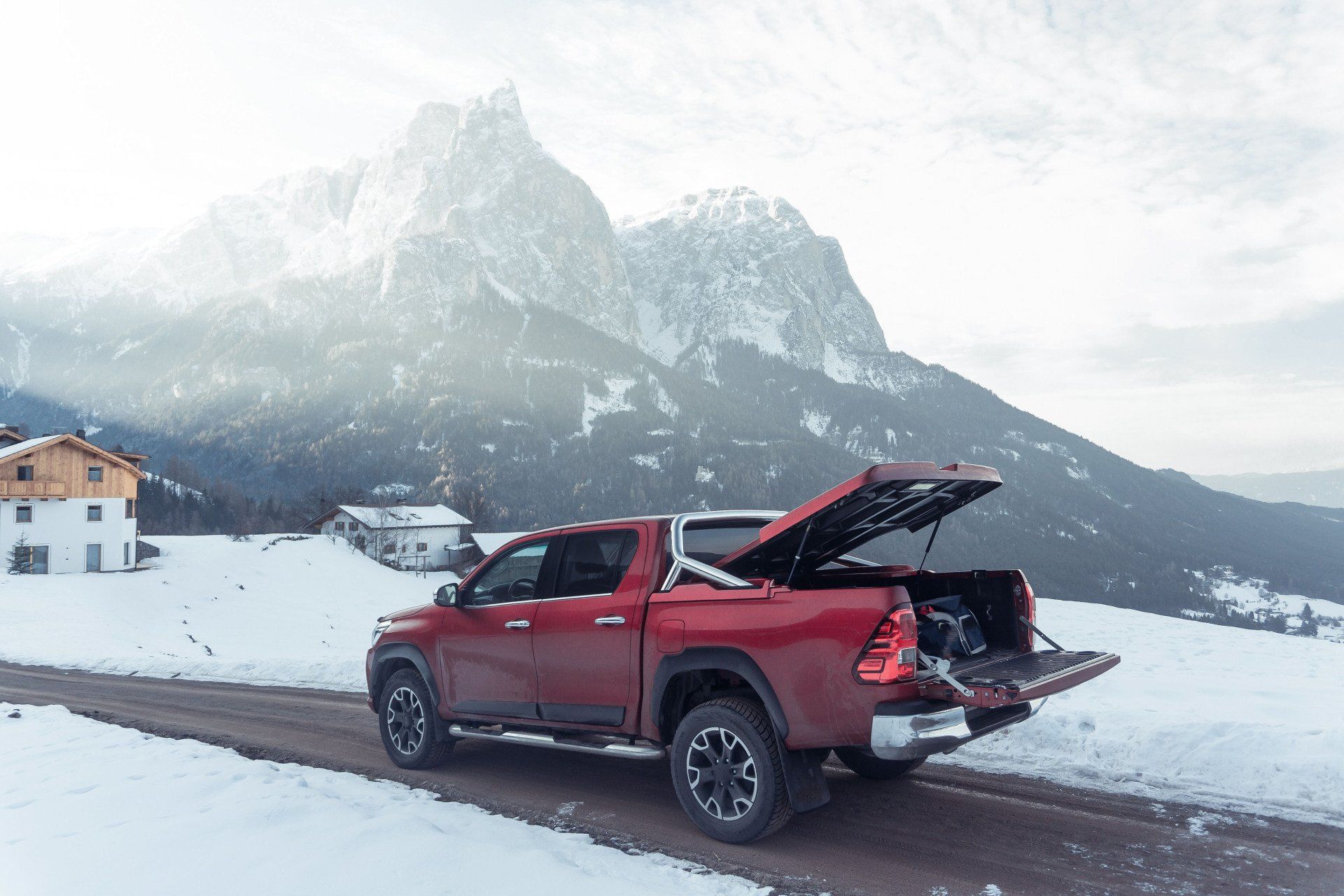 Red pickup truck with open tailgate on a snowy road, mountains in the background.