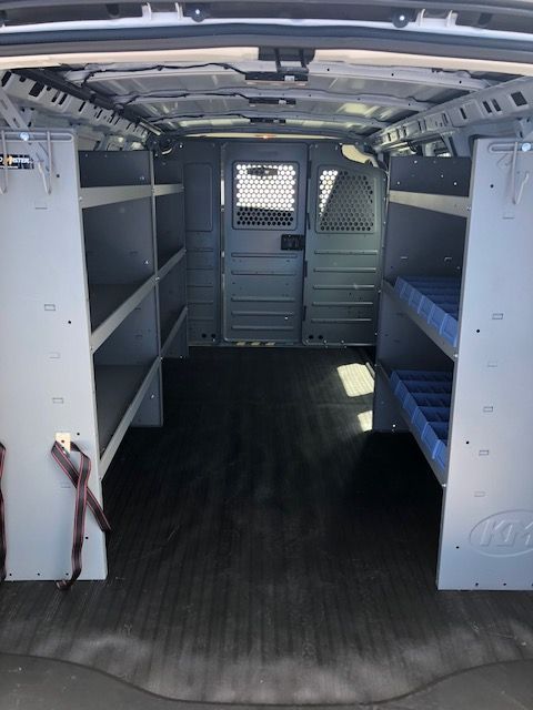 Empty white cargo van interior with shelving units and dark flooring.