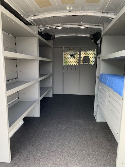 Interior of a white work van with shelving on both sides and a central partition. Gray flooring.