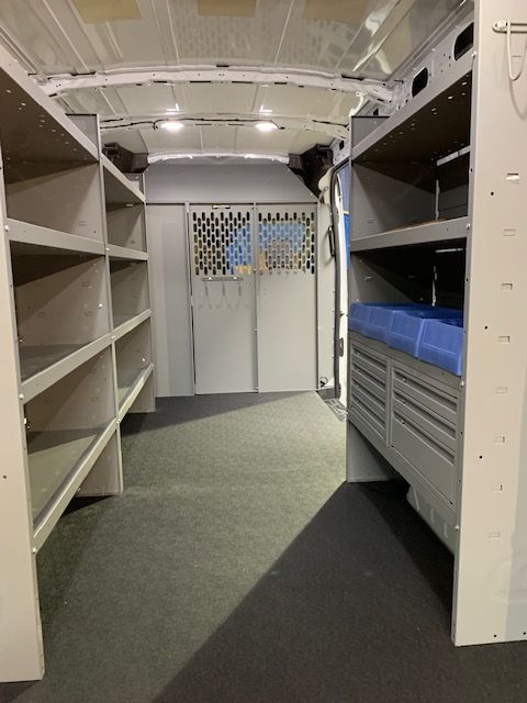 Interior of a cargo van with shelving on both sides and a partition wall in the back.