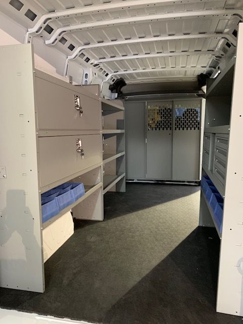 Interior of a white work van with gray shelving and storage compartments. Blue bins and black flooring are visible.