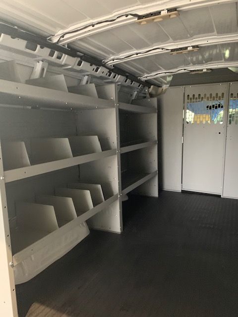 Interior of a white van with shelving units along the left side and a closed door on the right. Dark floor.