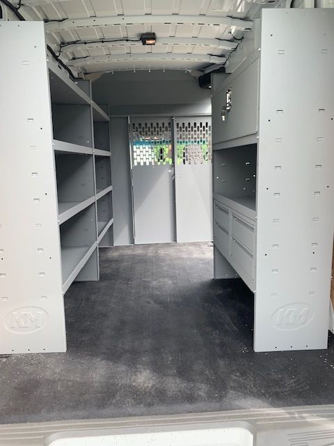 Interior of a cargo van with shelving units on both sides and two doors in the back.