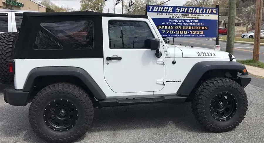 White Jeep Wrangler with black top and tires parked outside a Truck Specialties shop.