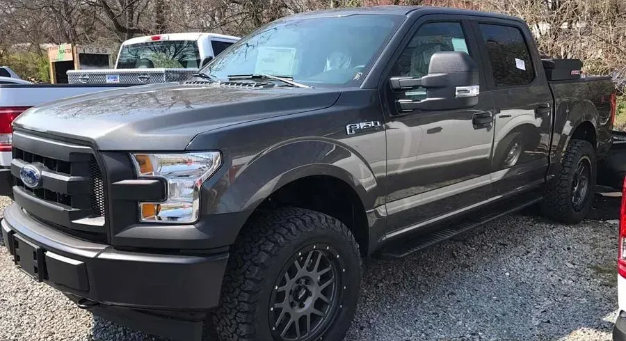 Dark gray Ford F-150 truck with black wheels and tires, parked outdoors on gravel.