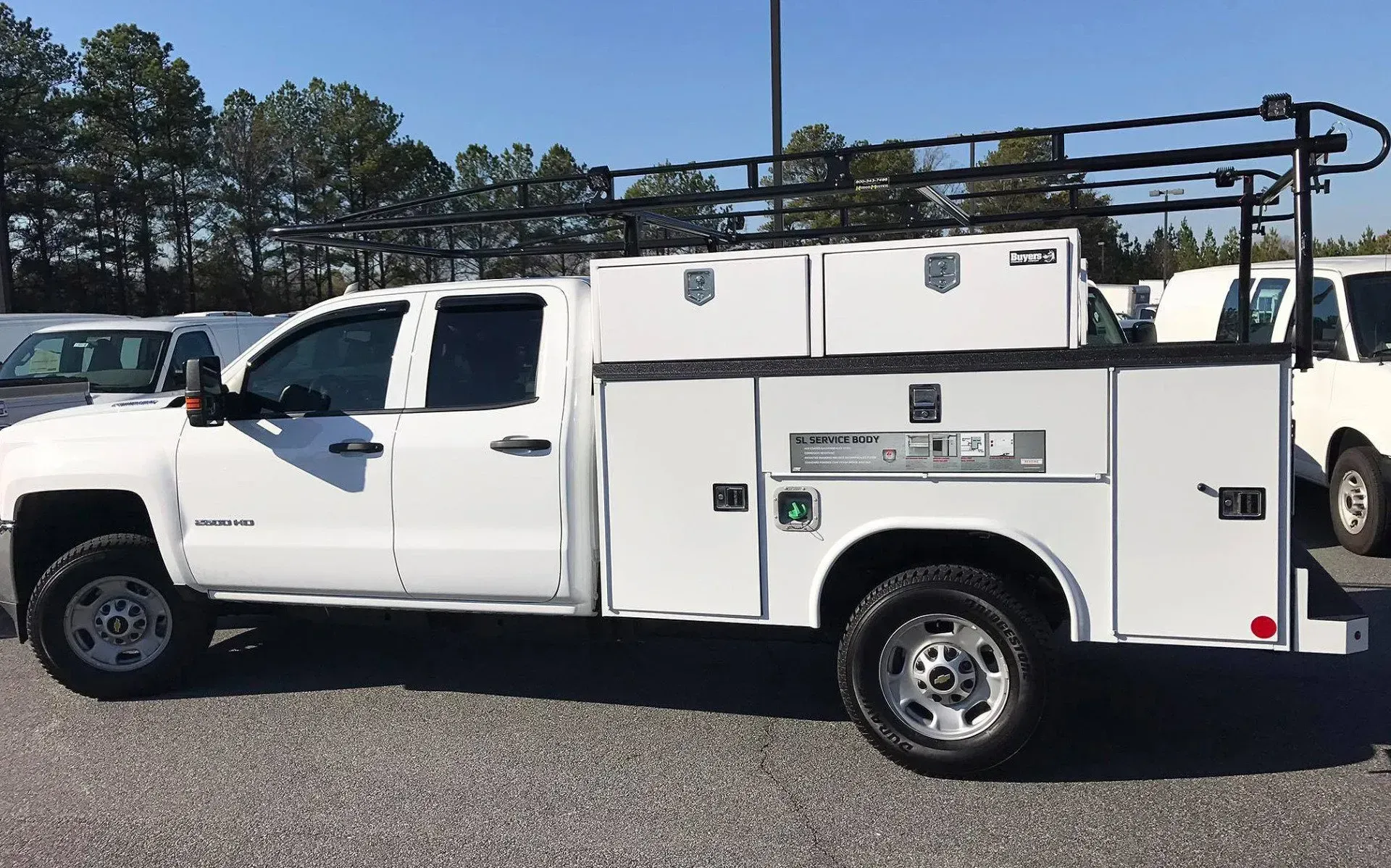 White service truck with ladder rack, storage compartments, and black roof rack.