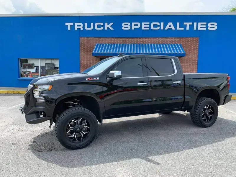 Black lifted Chevy Silverado truck parked in front of a blue