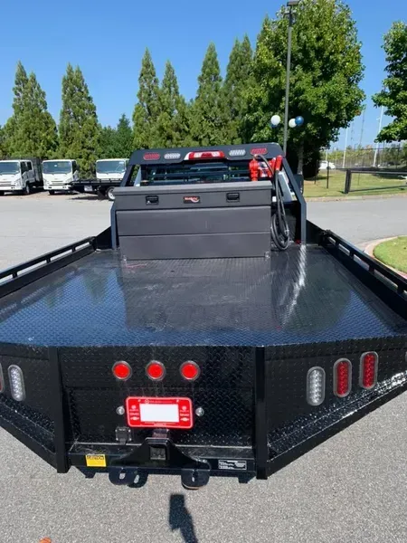 Black flatbed truck with diamond plate bed, tool box, and red lights in a parking lot.