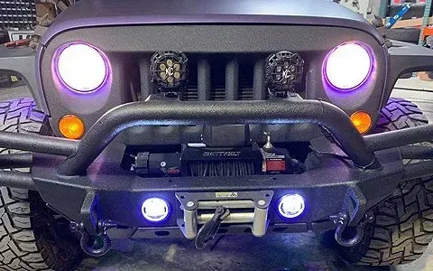 Black Jeep with purple-lit headlights, two additional lights, and a winch, set in a garage.