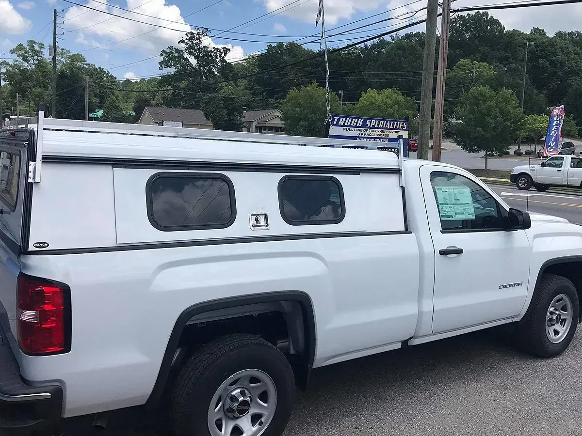 White pickup truck with a white camper shell, parked outside.