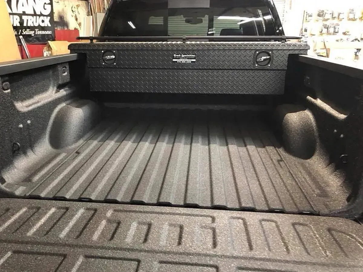 Black pickup truck bed with a black toolbox. The bed has a textured surface.