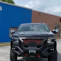 Black SUV with red grill parked in front of a blue building under a cloudy sky.
