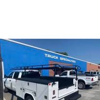 White work truck with a utility bed parked in front of a blue building with