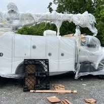 White utility truck with boom wrapped in plastic, sitting outside with a pallet.