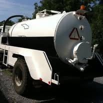 White and black cylindrical tank mounted on a truck chassis, parked outdoors.