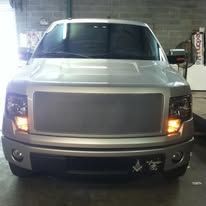A silver Ford truck with a custom grill and headlights. It is parked indoors.