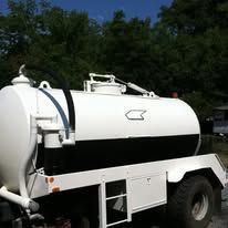 White and black tanker truck on a trailer, parked outdoors.
