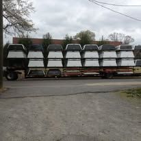 A long trailer loaded with a large number of white truck toppers, parked on a road.