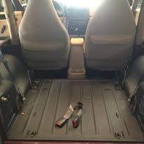 Interior of a Jeep with seats removed, showing the floor, including seatbelt buckles.