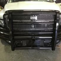 Black heavy-duty truck grille, part of a white truck. Close-up, the truck is outdoors.