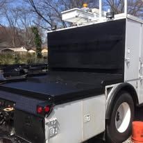 A utility truck with a black bed cover, parked outside, on a sunny day.