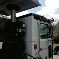 White truck cab with a metal exhaust pipe and mirrors against a cloudy sky.