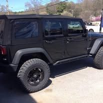 Black Jeep Wrangler with large tires parked on a paved surface on a sunny day.