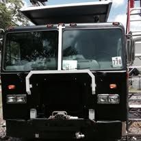 Black fire truck, front view, in daylight, with headlights and a raised platform.