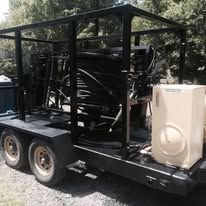 Black trailer with equipment, including hoses and a large white box.