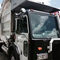 Black and white garbage truck cab; side view; against blue sky.