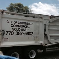 White garbage truck from City of Cartersville with phone number.