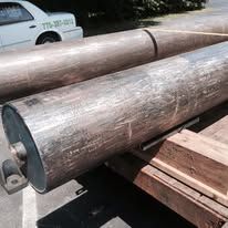 Large metal rollers, possibly industrial, on wooden supports, outdoors.