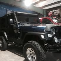 Dark blue Jeep with a light bar parked inside a garage.
