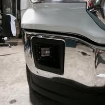 Close-up of a truck's front bumper with an installed black LED light in a chrome housing.