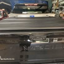 Black pickup truck bed with closed tonneau cover and toolbox.