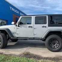 Silver Jeep parked in front of a blue building with black wheels.
