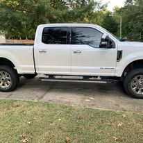 White Ford pickup truck parked on a driveway with trees in the background.
