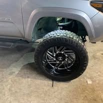 Close-up of a silver truck's front wheel, black and silver rim, off-road tire.