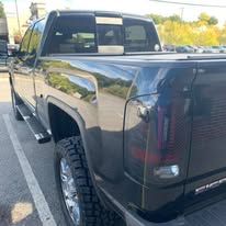 Black pickup truck parked outside, close-up of the rear with taillights and tires visible.