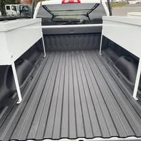 Truck bed with dark gray lining and white storage boxes on the sides.