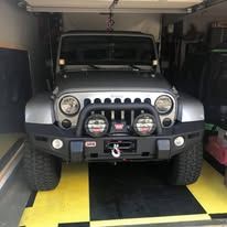 Silver Jeep Wrangler parked in a garage with black and yellow checkered floor.