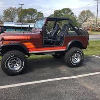 A vintage red Jeep parked outside. Black roll cage and tires with a brown body.