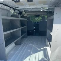 Interior of a white cargo van with empty shelving on the left and a view of the front seats.