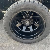 Black tire and rim with a Fuel logo, on a vehicle, outdoors.