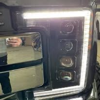 Close-up of a vehicle headlight with multiple lights and a bright white strip.