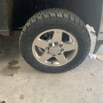Close-up of a truck tire and silver rim. The tire is black with a rugged tread pattern.